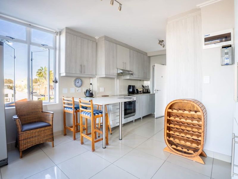 A functional kitchen featuring light wood-grain cabinetry, integrated appliances, tiled flooring, and a breakfast bar area with natural light from a large window.