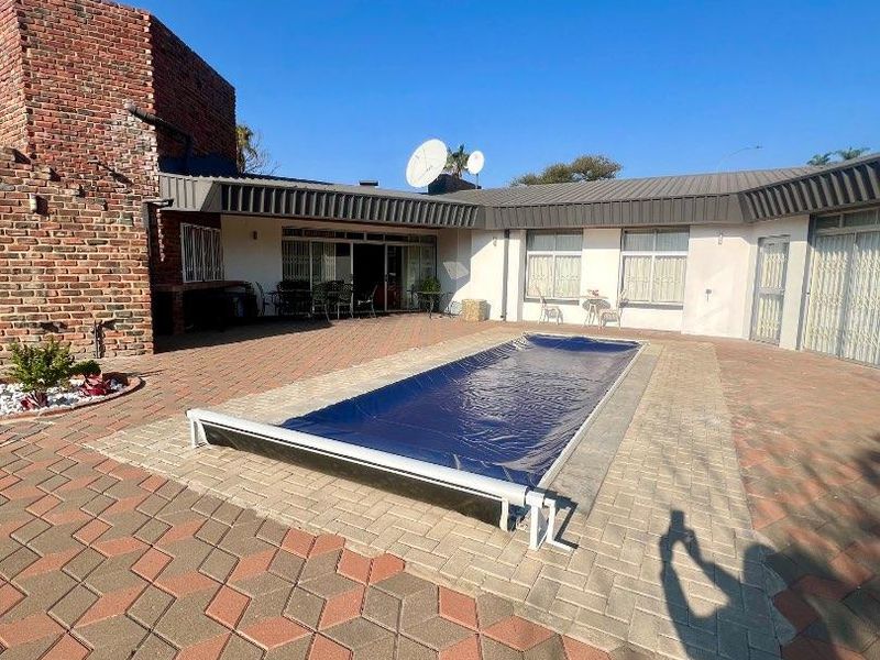 Outdoor pool area featuring a covered swimming pool, extensive brick paving, and a prominent brick chimney structure against the rear building facade.