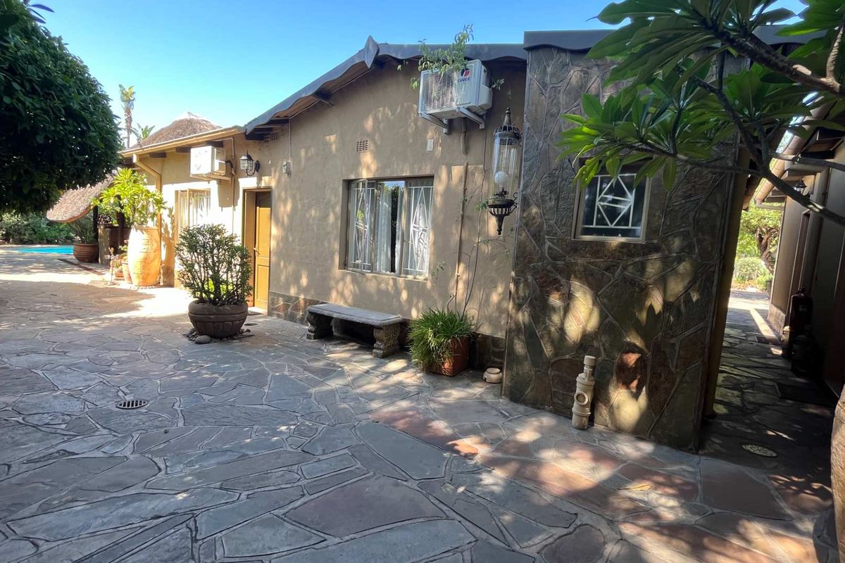A rear exterior view of the guest house featuring stone paving, stone-clad wall accents, and an outdoor patio area.
