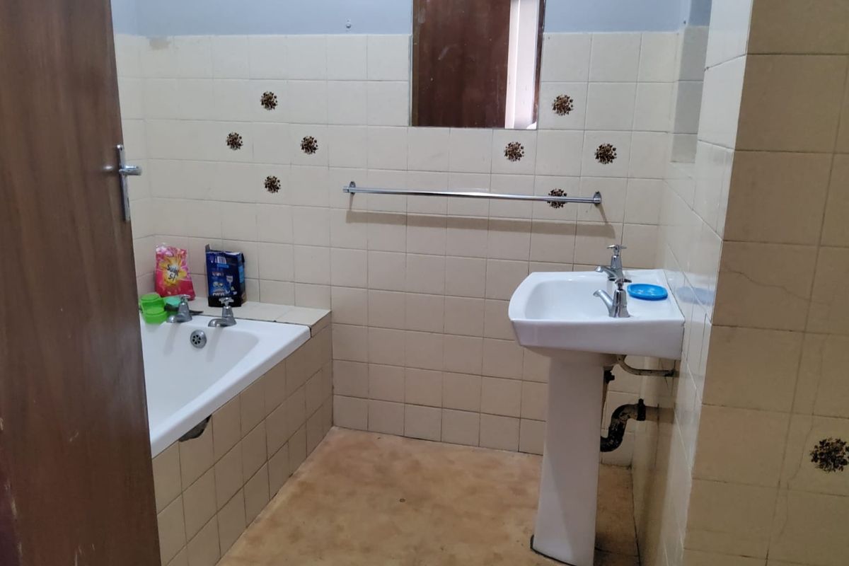 A dated bathroom featuring a built-in bathtub, pedestal basin, and wall-mounted towel rail, requiring cosmetic updates to modernize the space.