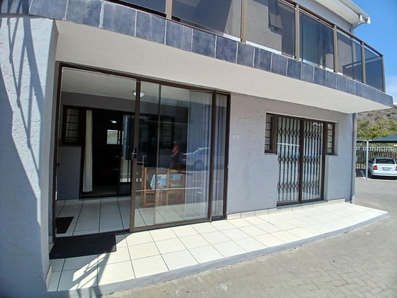 Front exterior view of the cluster unit featuring a tiled patio, sliding glass doors, security gates, and an upper-level balcony with a glass balustrade.
