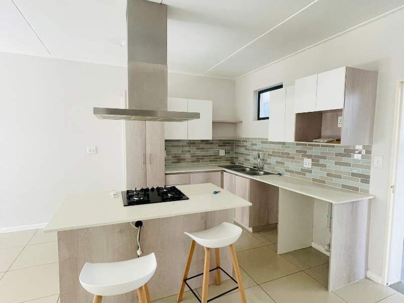 Modern kitchen featuring a central island with a gas hob, stainless steel extractor fan, tiled backsplash, and ample built-in cabinetry with tiled flooring.