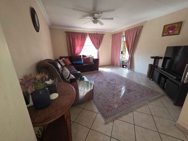 A living room featuring tiled flooring, a ceiling fan, and a sliding glass door providing access to the exterior.