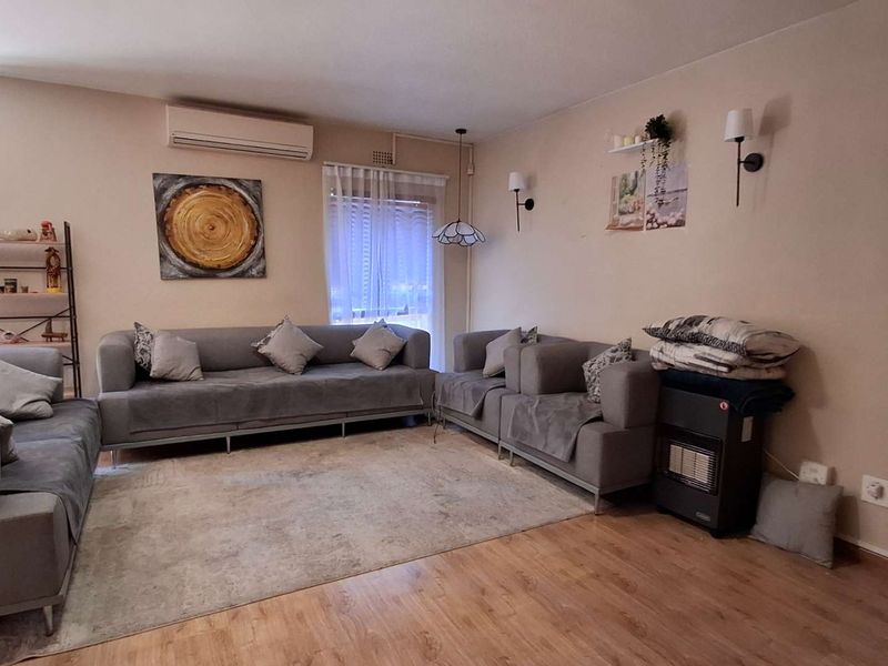A comfortable living room featuring laminate flooring, a wall-mounted air conditioning unit, and integrated wall lighting.