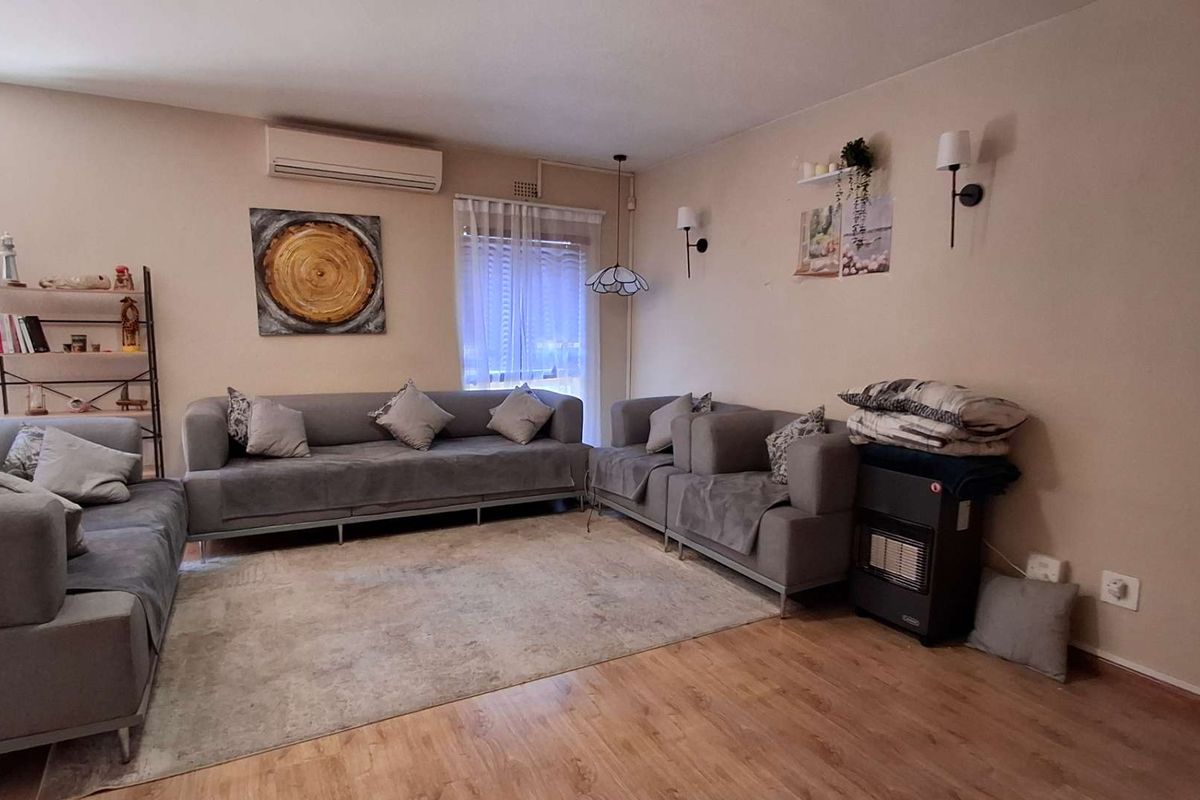 A comfortable living room featuring laminate flooring, a wall-mounted air conditioning unit, and integrated wall lighting.