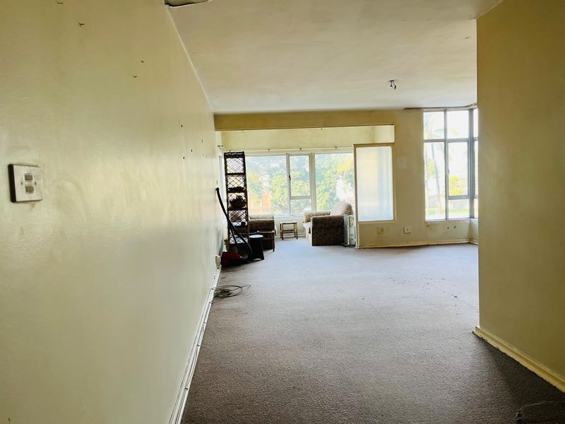 Spacious living area featuring large windows, carpeted flooring, and significant potential for renovation to restore the interior finishes.