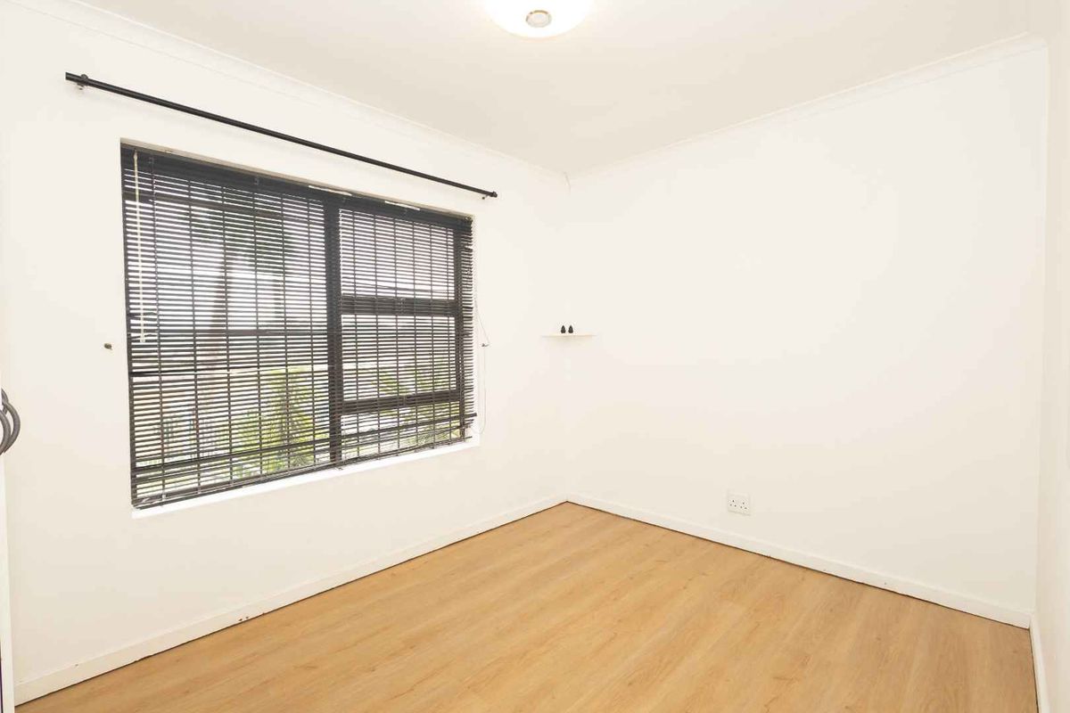 A bright, empty bedroom featuring light-toned laminate flooring, neutral walls, and fitted venetian blinds, providing a clean and versatile space.