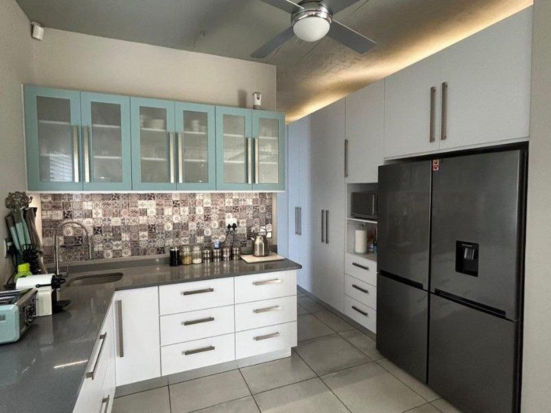 Modern kitchen featuring two-tone cabinetry, stone countertops, decorative tiled backsplash, integrated microwave, and large format floor tiles.