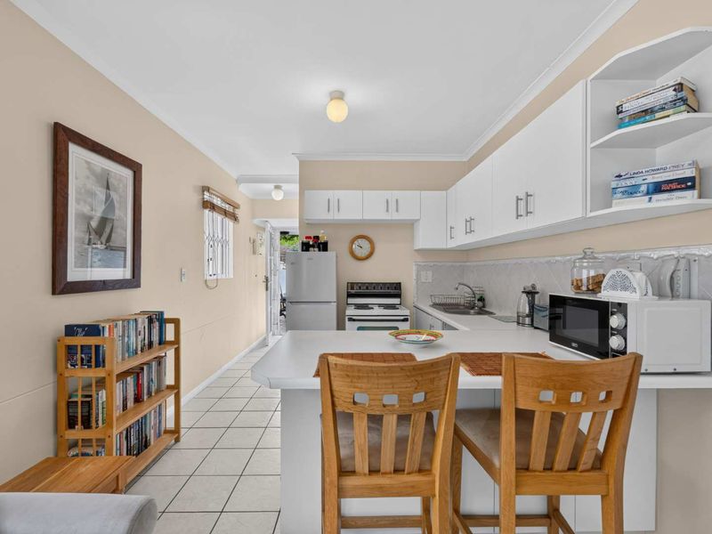 A functional kitchen featuring white cabinetry, laminate countertops, a freestanding stove, and tiled flooring, with an integrated breakfast bar area.