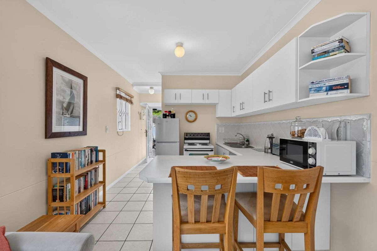 A functional kitchen featuring white cabinetry, laminate countertops, a freestanding stove, and tiled flooring, with an integrated breakfast bar area.