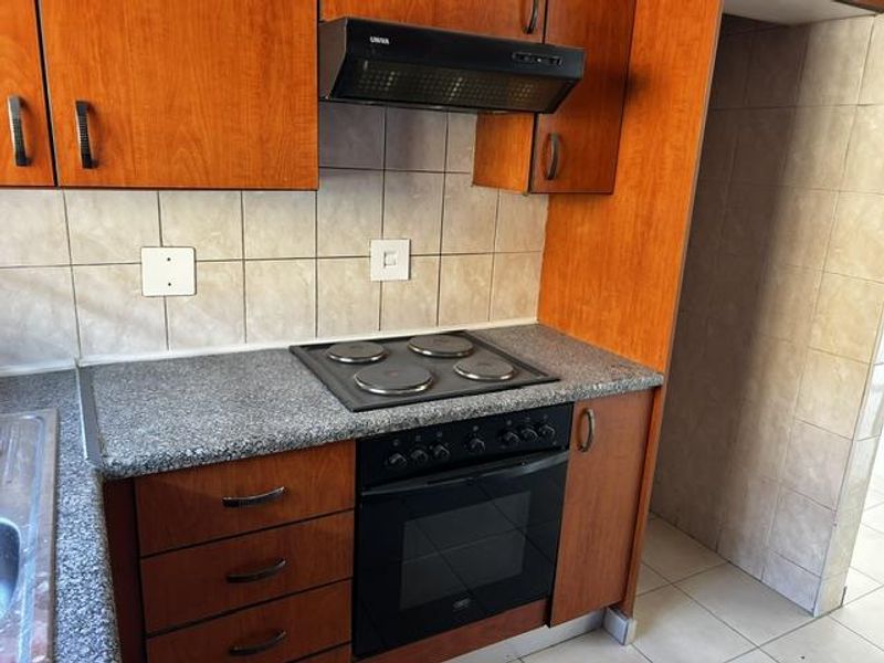 A functional kitchen featuring wood-finish cabinetry, granite-look laminate countertops, a built-in electric oven and hob, and a tiled backsplash.