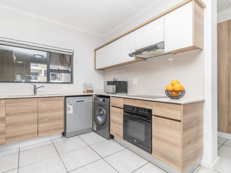 Modern kitchen featuring wood-finish cabinetry, white upper cabinets, integrated appliances, electric oven with hob, and tiled flooring.