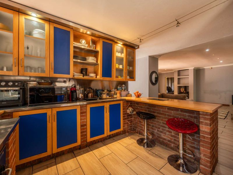A kitchen featuring wooden and blue cabinetry, a brick breakfast bar with a wooden countertop, and tiled flooring, opening into an adjacent living area.