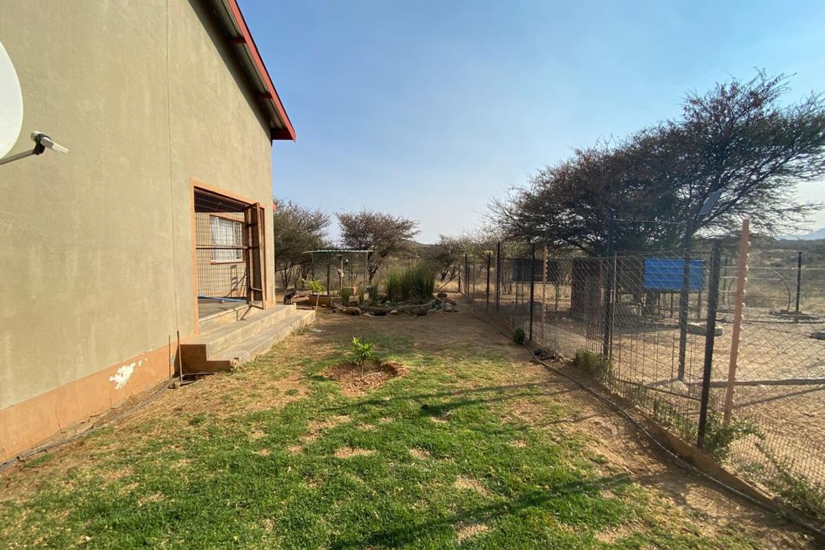 A side garden area featuring a lawn, perimeter wire fencing, and direct access to the house via a side door.