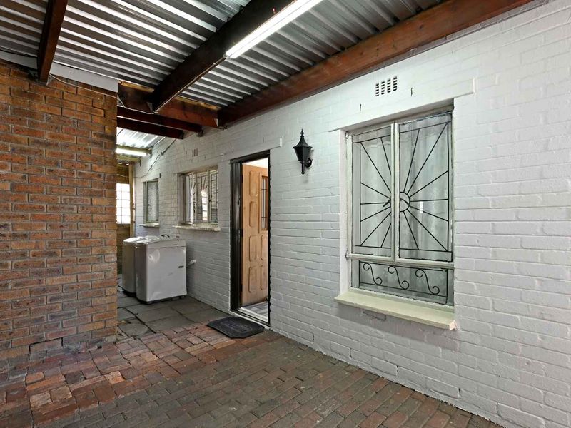 A covered outdoor patio area featuring exposed brick walls, timber beam ceiling, and brick paving, providing a functional transition space.
