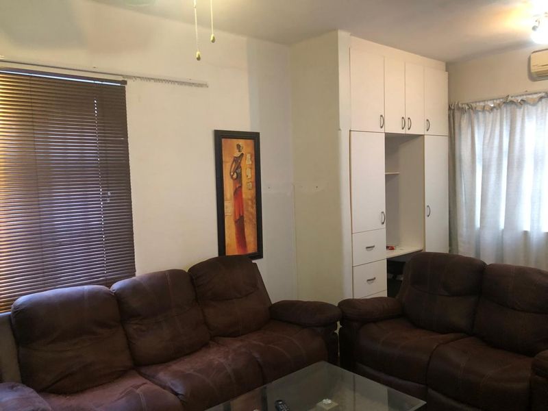 A living room featuring built-in white cabinetry, venetian blinds, and an air conditioning unit, offering a functional space with potential for cosmetic updates.