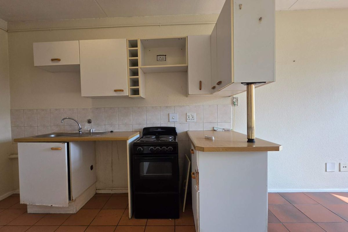 A compact kitchen featuring basic white cabinetry, a tiled backsplash, a freestanding stove, and a stainless steel sink with tiled flooring.