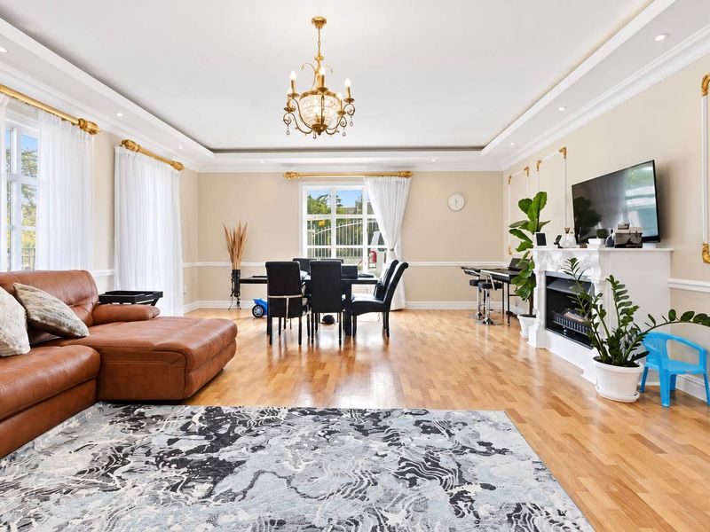 Spacious open-plan living and dining area featuring hardwood flooring, decorative wall molding, a fireplace, and elegant recessed ceiling lighting.