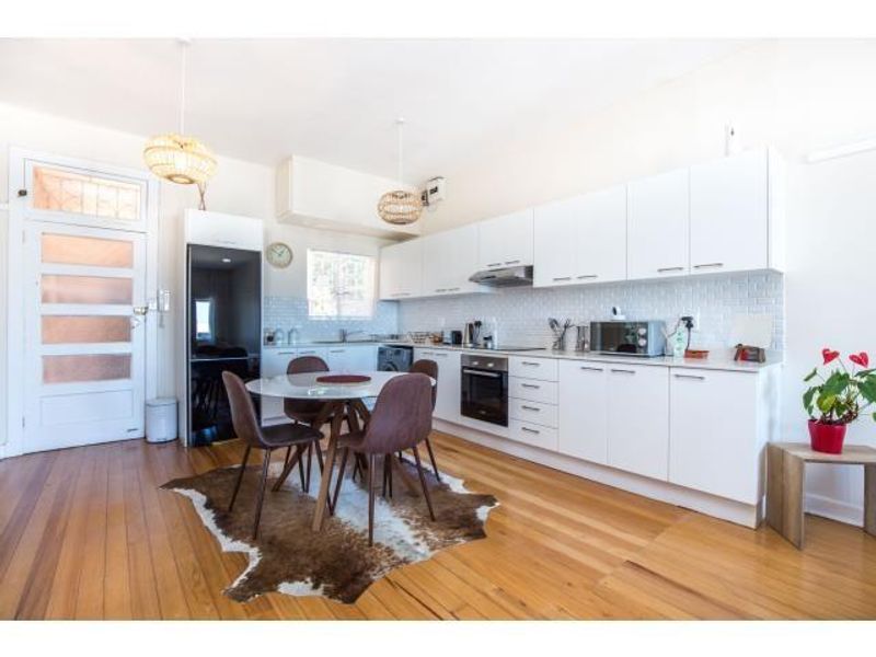 Bright open-plan kitchen and dining area featuring modern white cabinetry, subway tile backsplash, built-in appliances, and warm hardwood flooring.