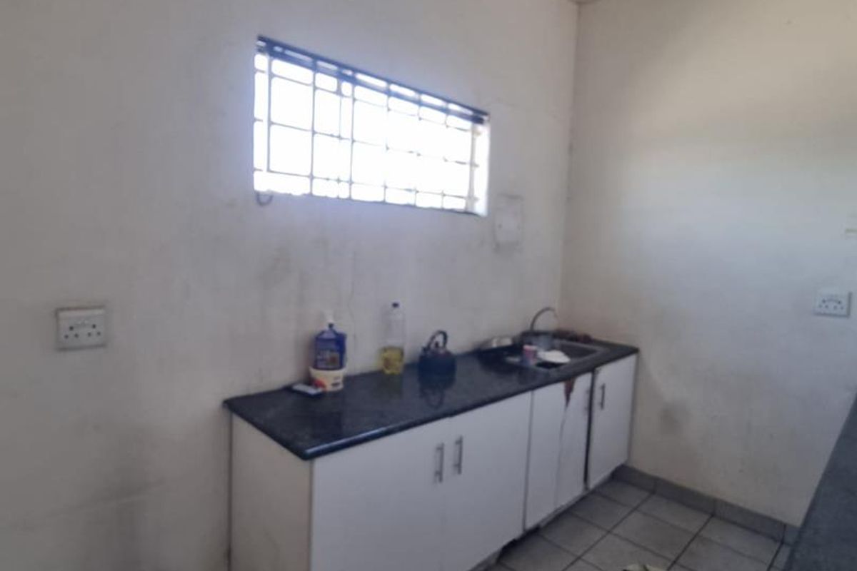A functional kitchen area featuring granite countertops, built-in cabinetry, a stainless steel sink, and tiled flooring, requiring cosmetic updates to improve its overall condition.