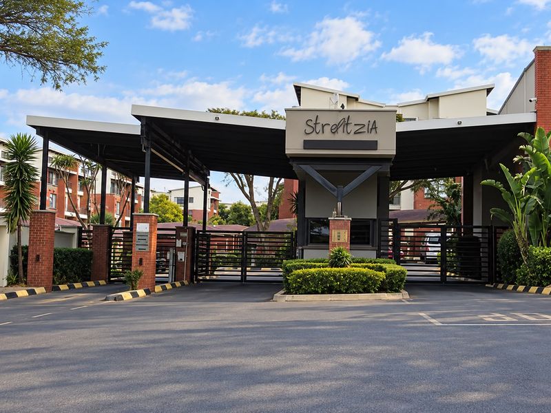 The main entrance to the Strelitzia apartment complex, featuring a secure gated access point, guard house, and covered driveway canopy.