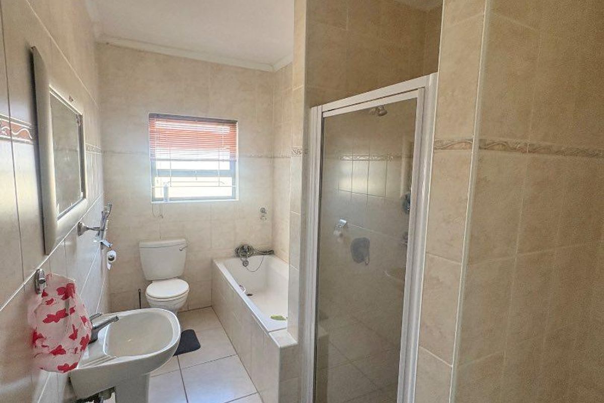 A functional bathroom featuring a pedestal sink, a built-in bathtub, and a separate glass-enclosed shower stall with neutral wall and floor tiling.
