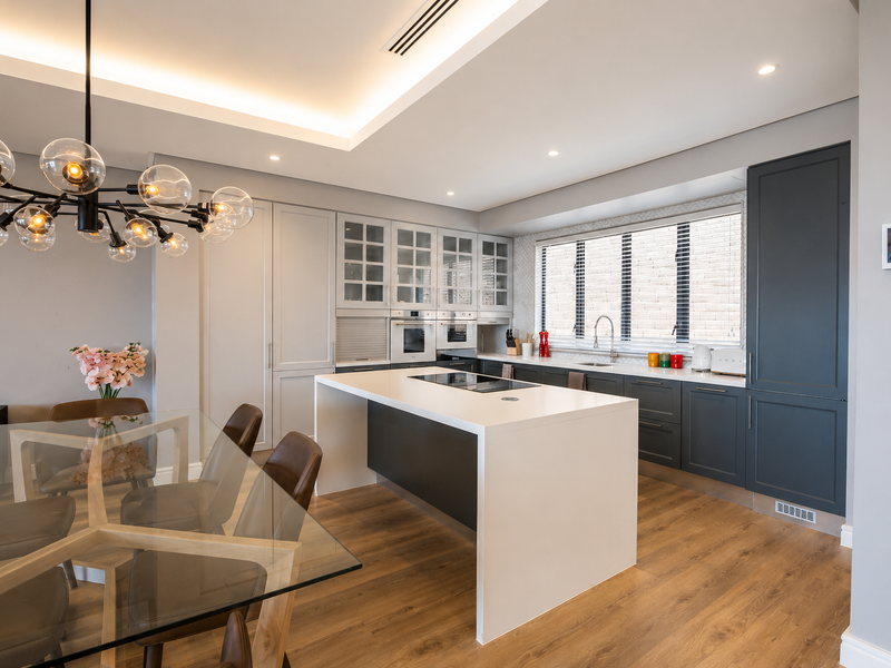 Modern open-plan kitchen and dining area featuring a central island, high-end built-in appliances, sleek cabinetry, and sophisticated recessed and cove lighting.