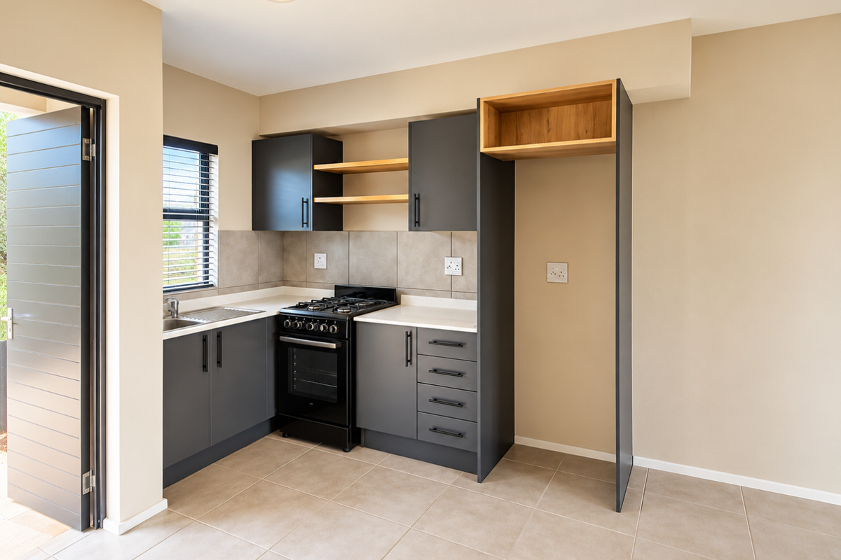 A modern, clean kitchen featuring dark grey cabinetry, quartz countertops, a gas stove with oven, and neutral tiled flooring with direct outdoor access.