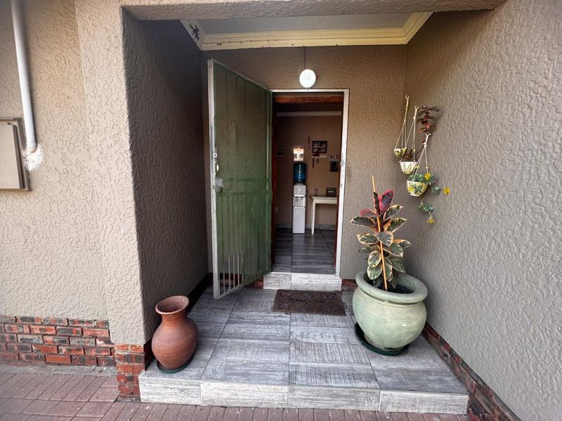 Covered entrance porch featuring tiled flooring, a security gate, and textured exterior walls, providing a functional and welcoming access point to the home.
