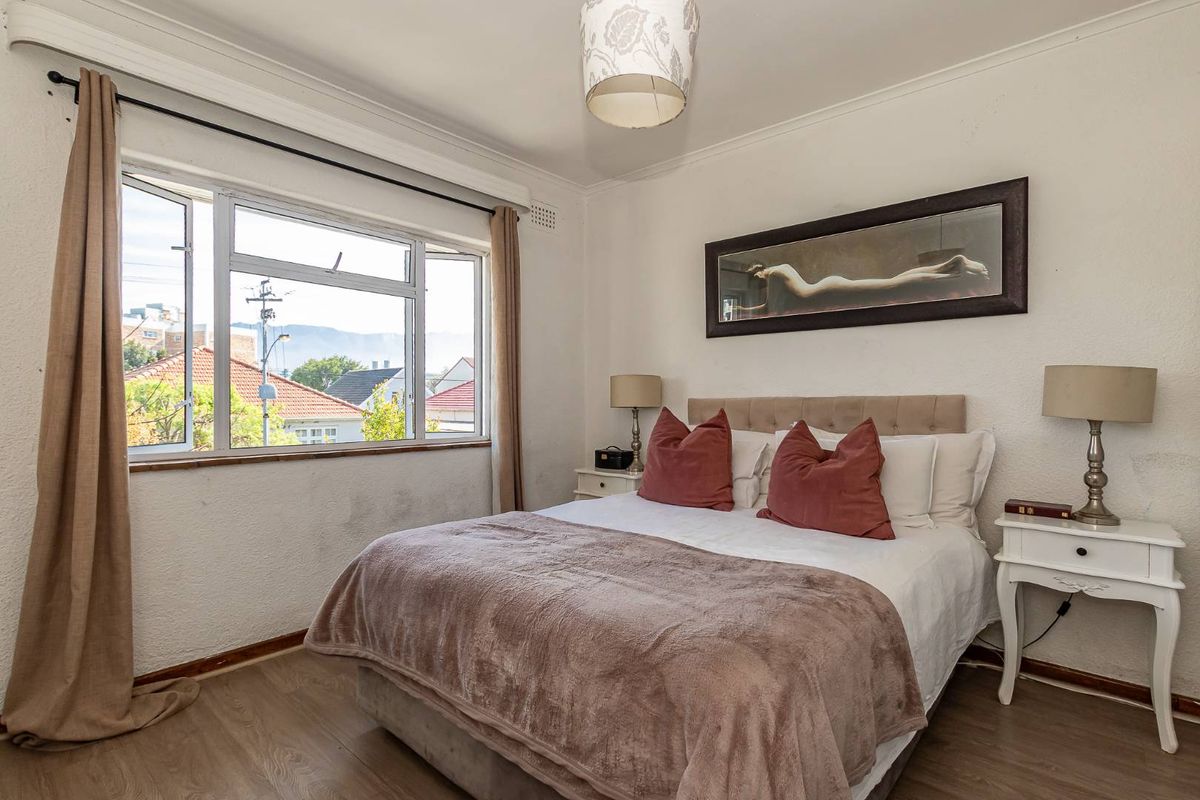 A well-lit bedroom featuring laminate flooring, coved ceilings, and a large window with views of the surrounding neighborhood.