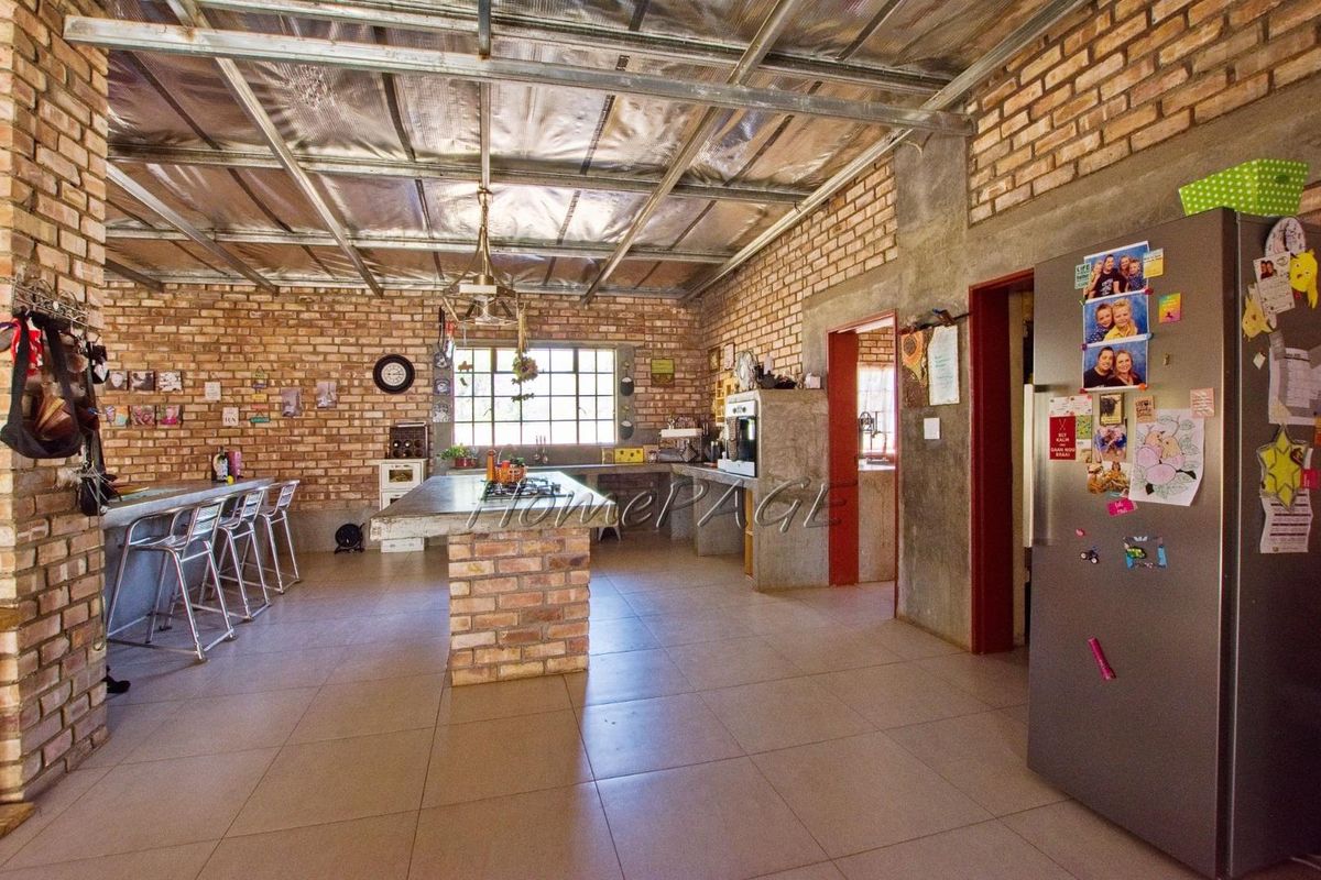 Spacious industrial-style kitchen featuring exposed brick walls, a central brick island with a built-in cooktop, and tiled flooring.