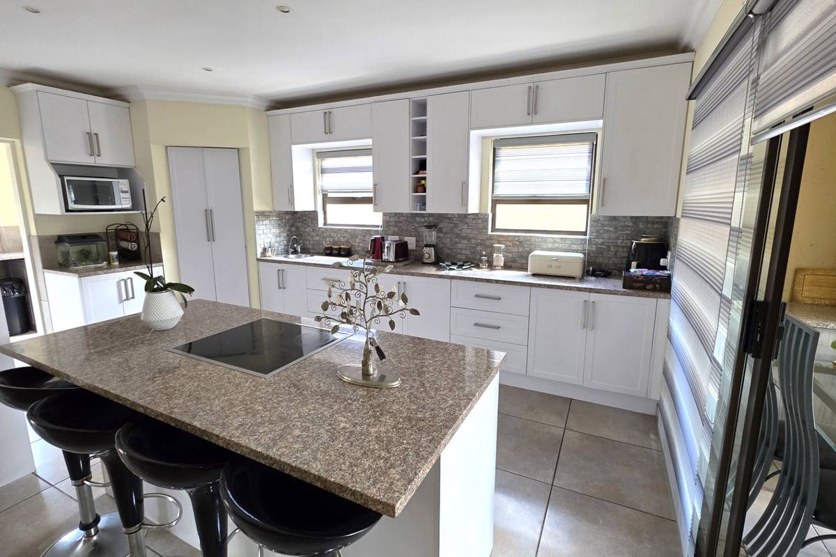 Modern kitchen featuring white cabinetry, granite countertops, a central island with an integrated induction hob, and tiled flooring.