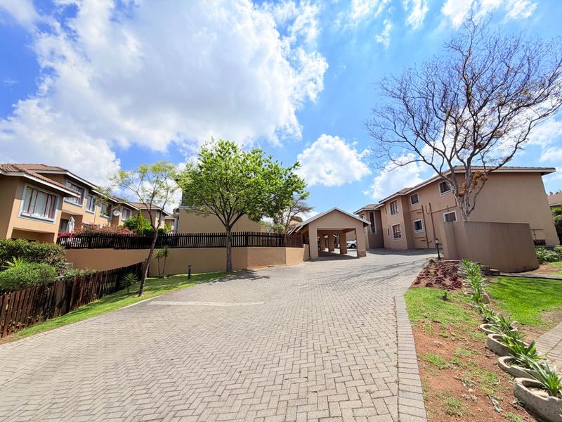A wide-angle view of the apartment complex entrance, featuring a paved driveway, covered carport, and well-maintained exterior building facades.