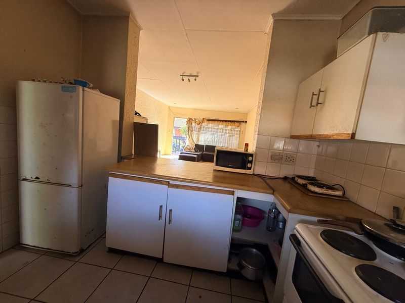 Open plan kitchen and living area featuring tiled flooring, built-in cabinetry, and electric stove, offering a functional layout with potential for modernization.