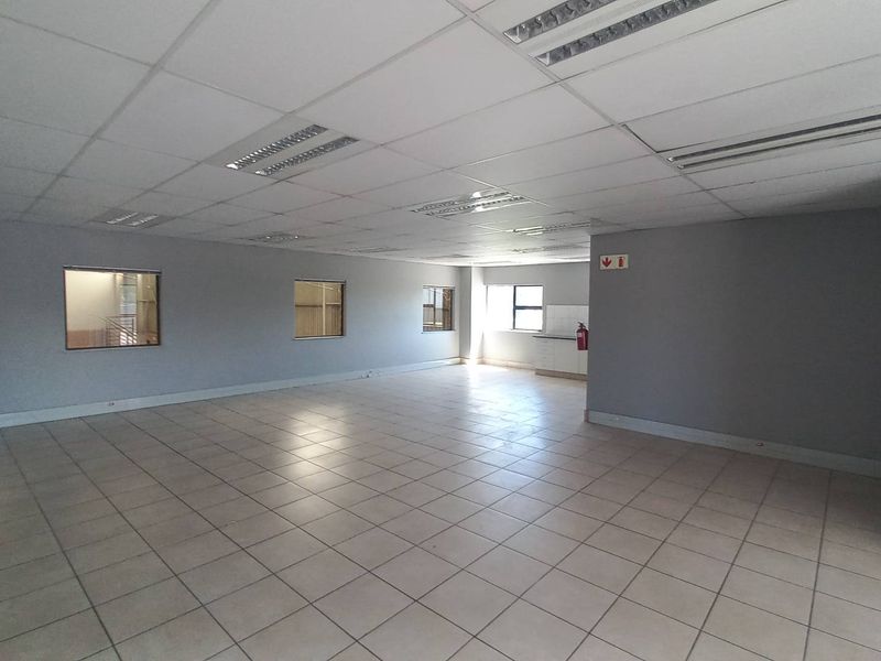 Spacious open-plan industrial office area featuring ceramic floor tiles, a suspended ceiling with recessed lighting, and internal windows providing natural light.