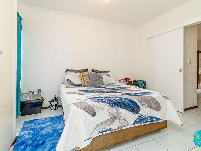 A functional bedroom featuring tiled flooring, a built-in wardrobe with a sliding door, and neutral wall finishes.