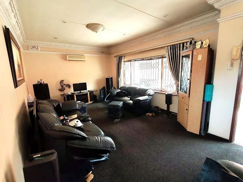 Spacious living room featuring decorative ceiling cornices, a split-system air conditioner, and large windows with security bars.