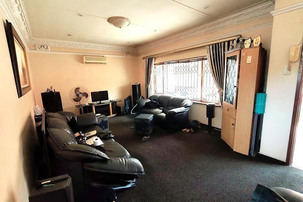 Spacious living room featuring decorative ceiling cornices, a split-system air conditioner, and large windows with security bars.