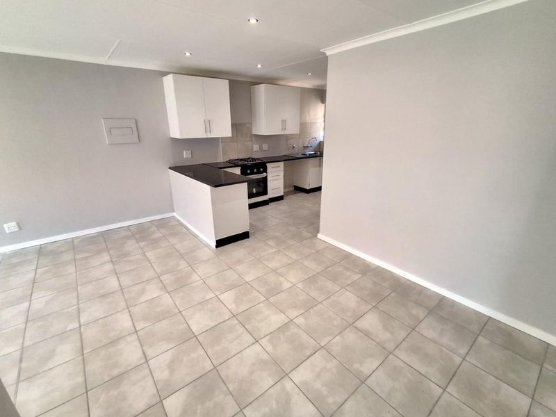 An open-plan kitchen and living area featuring neutral tiled flooring, modern cabinetry, a built-in oven and hob, and recessed downlighting.