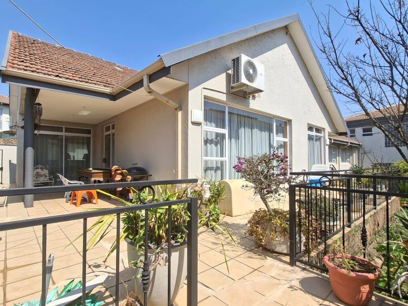 Rear exterior view of the townhouse featuring a tiled patio, built-in braai area, and secure wrought iron fencing.