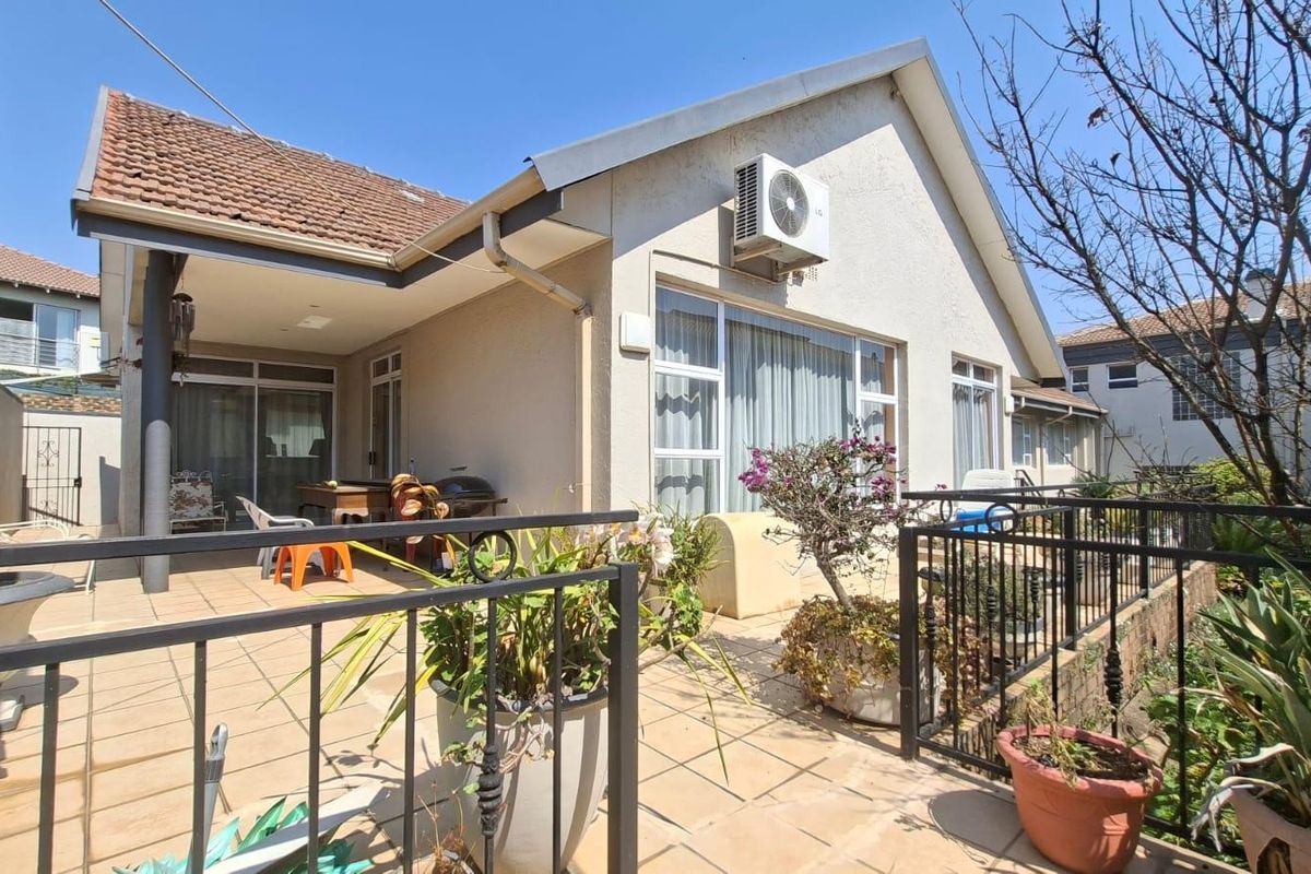 Rear exterior view of the townhouse featuring a tiled patio, built-in braai area, and secure wrought iron fencing.