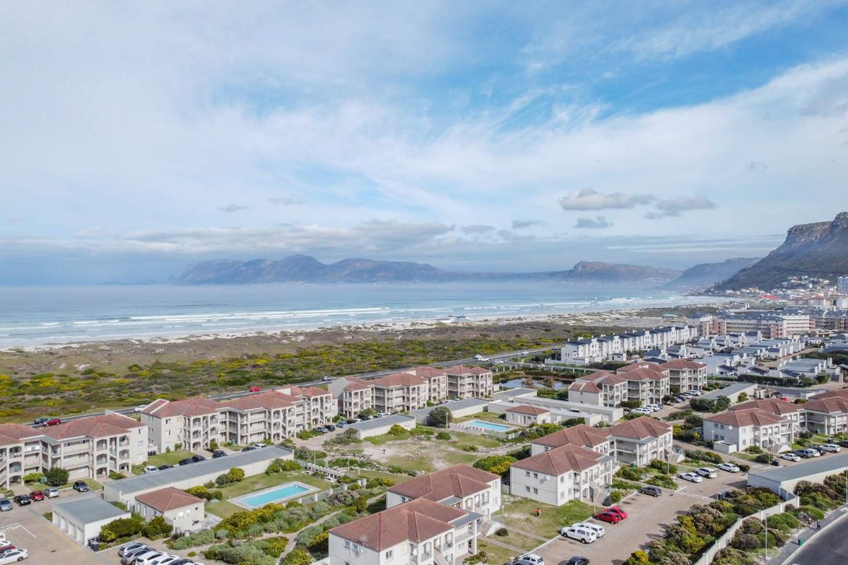 Aerial view of the apartment complex featuring multiple buildings, swimming pools, and proximity to the coastline and mountain range.