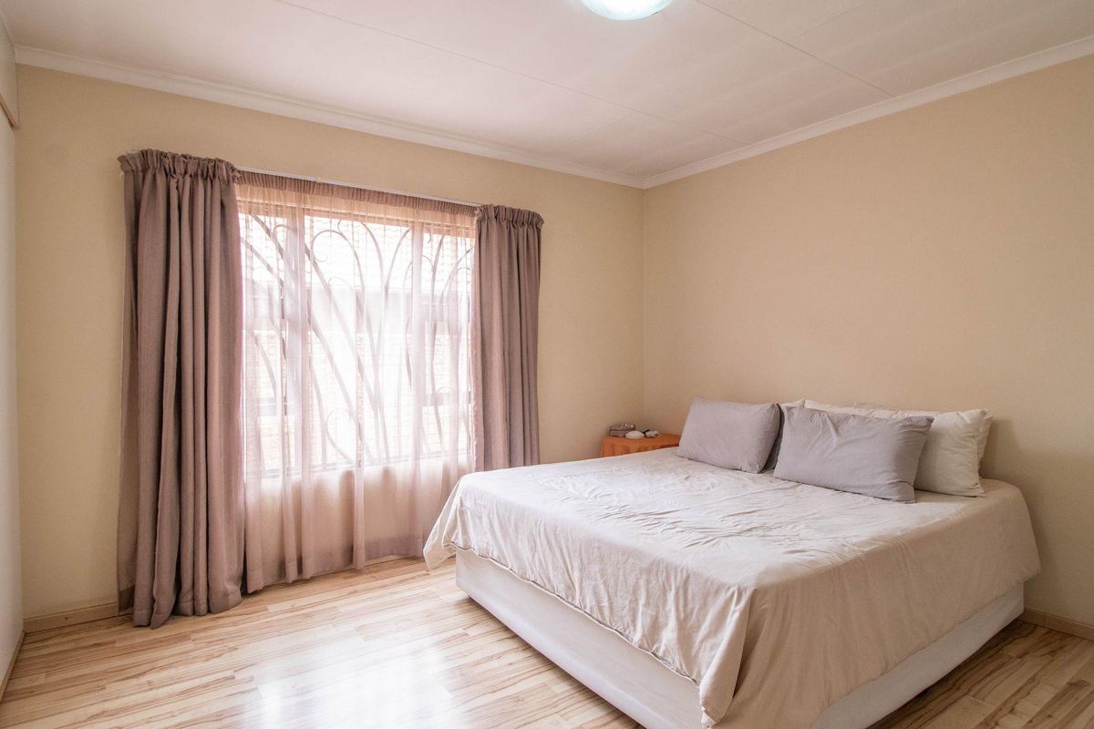 A well-lit bedroom featuring light-toned wood-look flooring, built-in cupboards, and a window fitted with security bars.