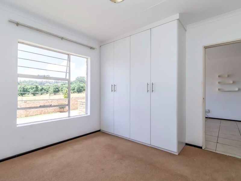 A bright, empty bedroom featuring built-in white cupboards, large windows with security bars, and neutral carpeting, offering a clean canvas for personalization.