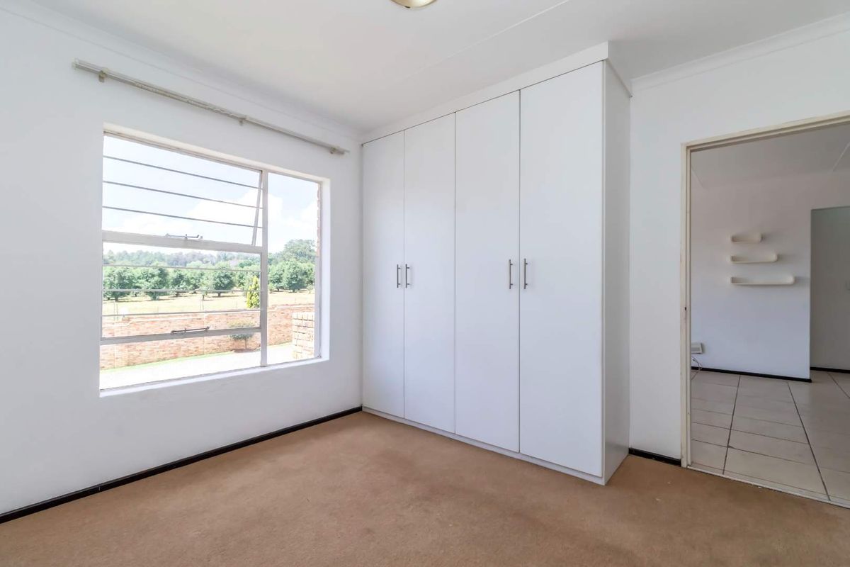 A bright, empty bedroom featuring built-in white cupboards, large windows with security bars, and neutral carpeting, offering a clean canvas for personalization.
