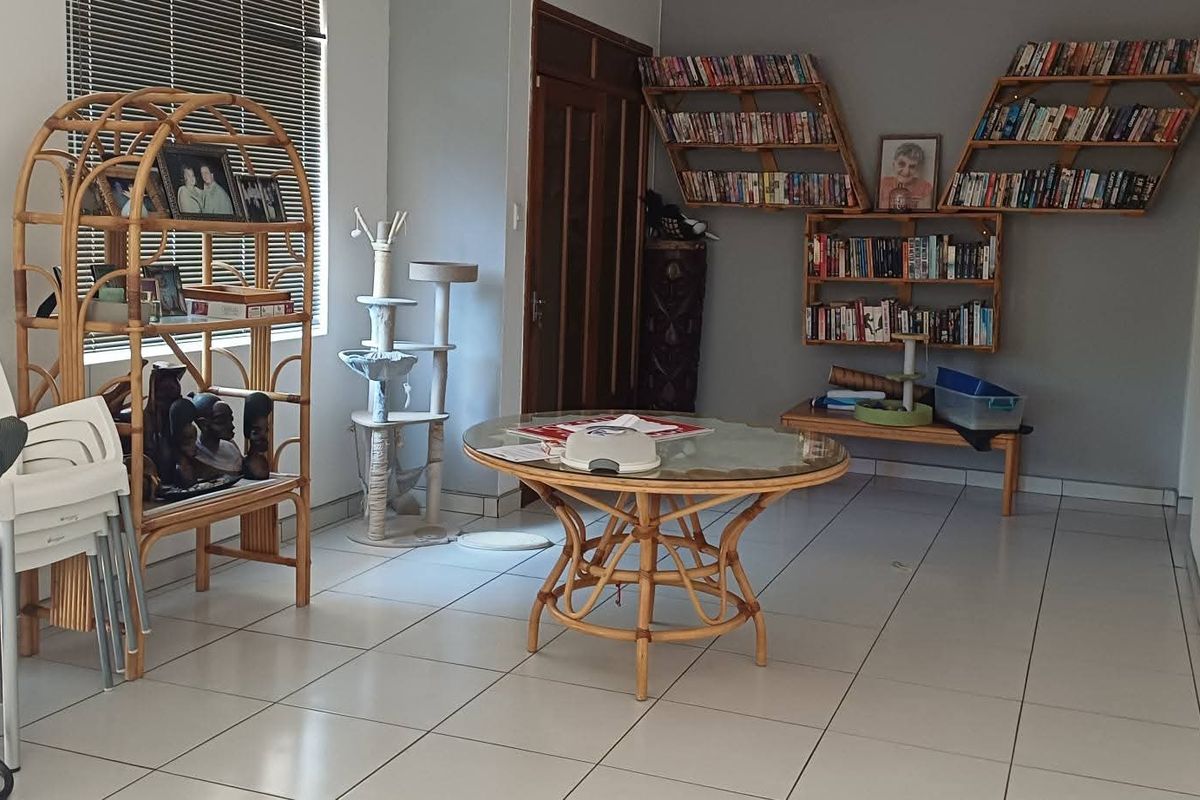A living area featuring tiled flooring, venetian blinds, and custom built-in wall shelving, providing a functional space with neutral wall finishes.
