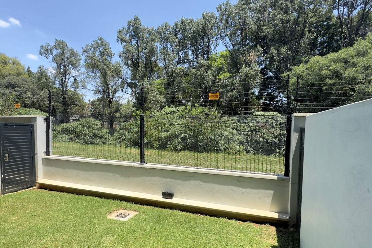 A private rear garden area featuring a manicured lawn, perimeter wall with integrated electric fencing, and a secure metal access gate.