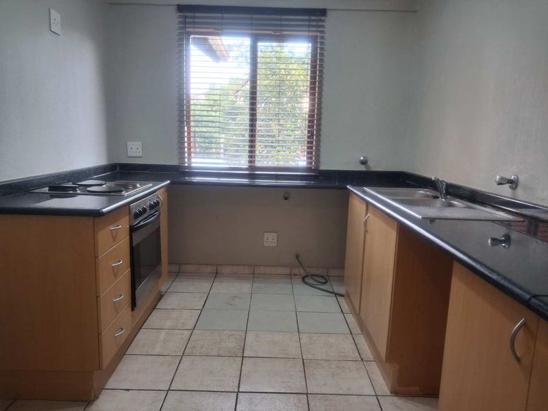 A functional kitchen featuring granite countertops, built-in oven, electric hob, and double sink with ample cabinetry and tiled flooring.