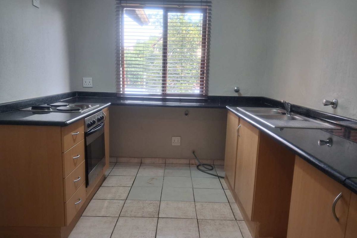 A functional kitchen featuring granite countertops, built-in oven, electric hob, and double sink with ample cabinetry and tiled flooring.