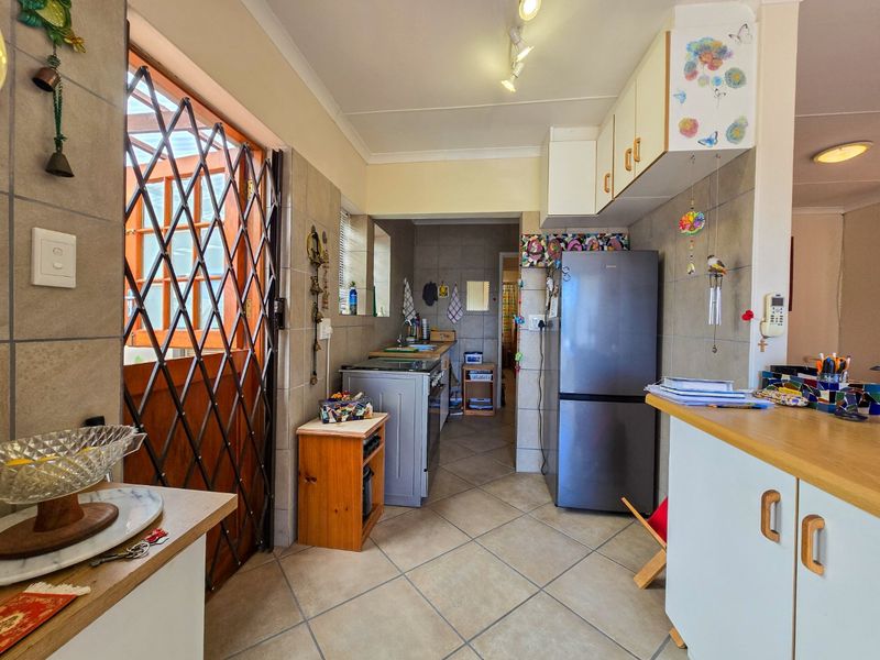 A functional kitchen featuring tiled flooring, wall-mounted cabinetry, and laminate countertops, with direct access to an outdoor area through a security gate.